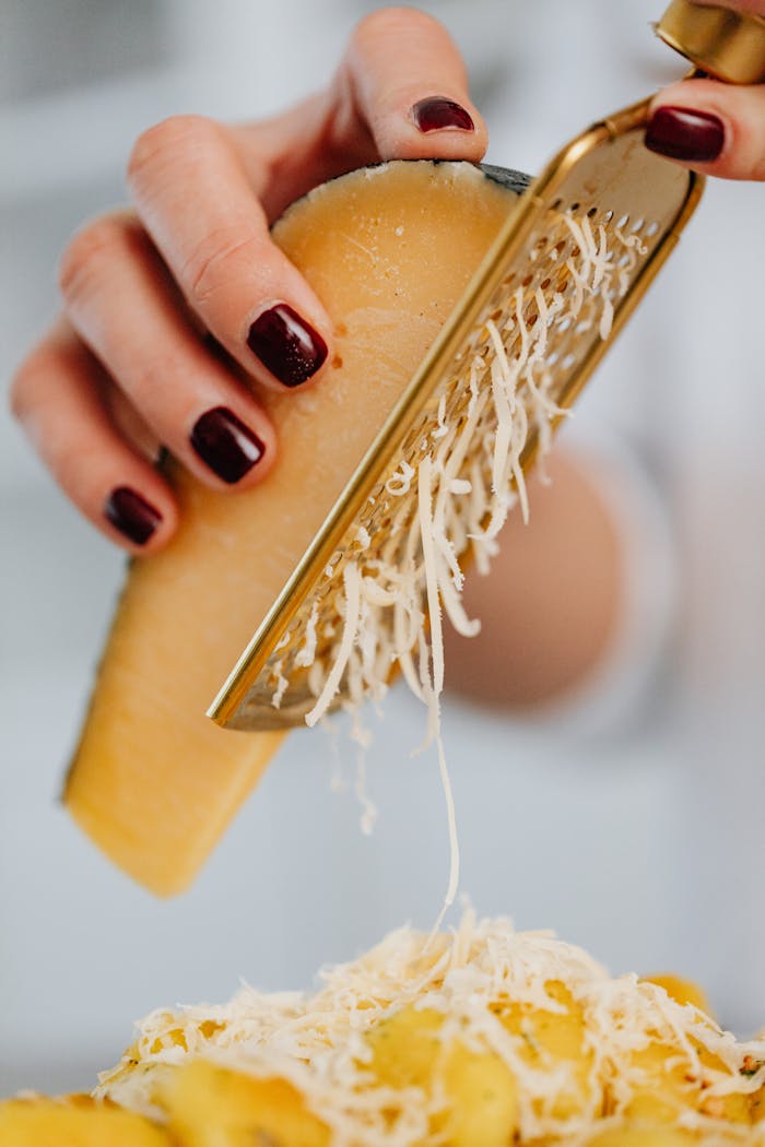 A hand grates Parmesan cheese onto pasta, showcasing detailed texture and fresh food preparation.