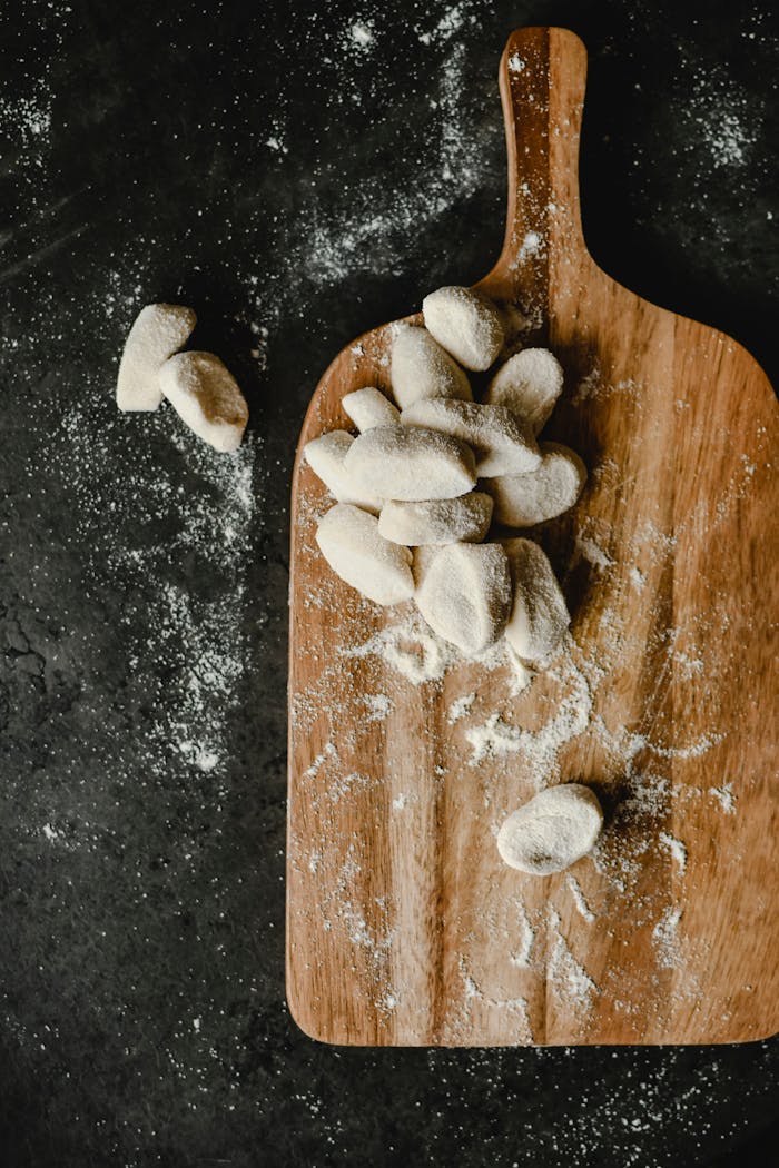 Rustic wooden board with fresh dough dumplings ready for cooking.